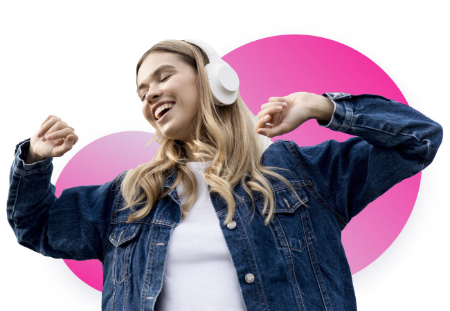 A young blonde woman wearing a denim jacket and white headphones, smiling with her eyes closed as she dances. She is against a white background with two large pink circles.