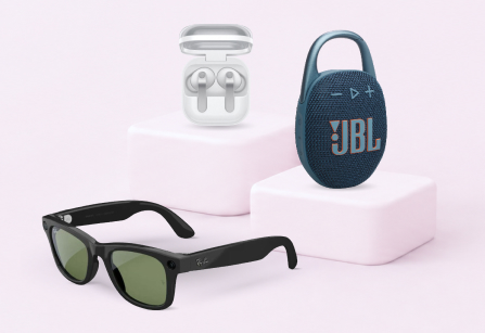 A product collage on a pale pink background featuring black Ray-Ban smart sunglasses in the foreground, white wireless earbuds in an open case on a pink block, and a blue JBL portable speaker on an adjacent block.