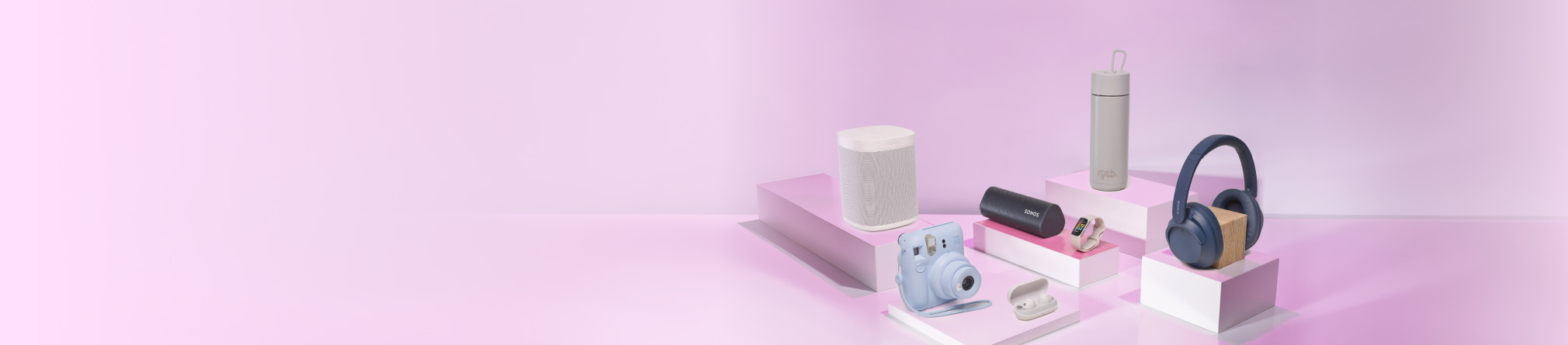 A collection of electronic gadgets and accessories are arranged on white rectangular platforms against a pink and purple gradient background.