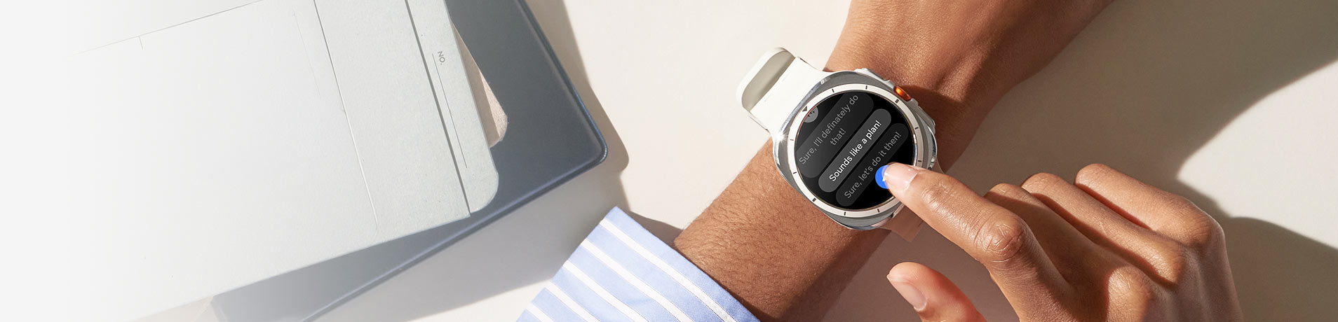 An overhead shot shows a person's arm wearing a white Samsung Galaxy watch7 on their left wrist, with their right index finger touching the watch face. The watch displays a thread of messages.