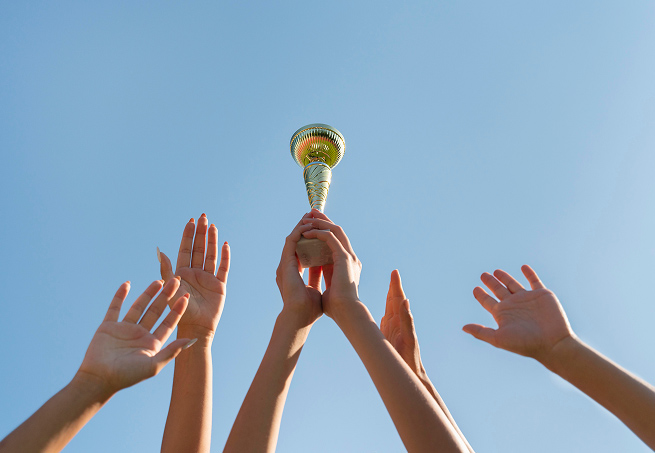 Hands holding up a trophy against a blue sky in celebration of a team victory.