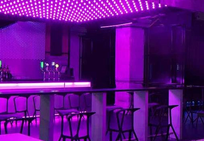 A bar area lit entirely in purple with stools and an LED ceiling