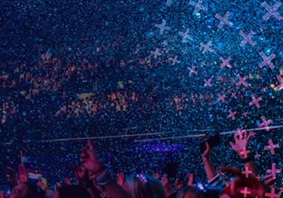 Crowd celebrating at a live event as blue confetti fills the arena.