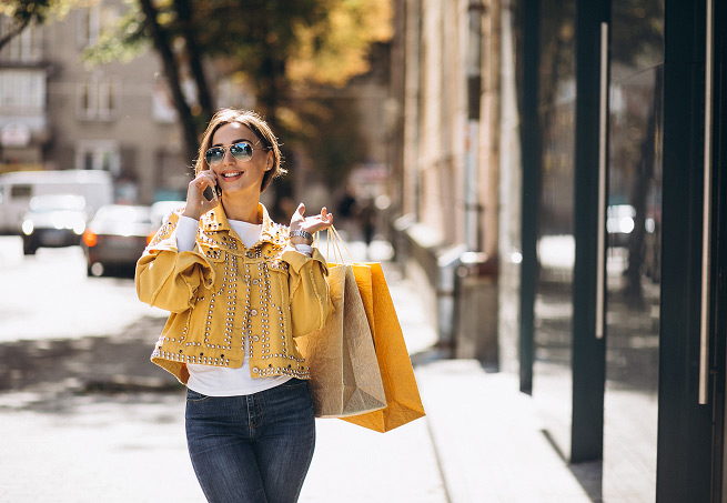 A woman in a yellow jacket talking on her phone while carrying shopping bags on a city street