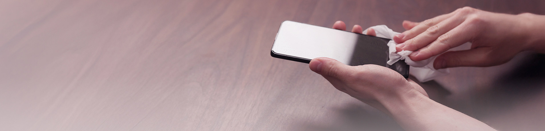 Hands wiping a smartphone screen clean with a white wipe.