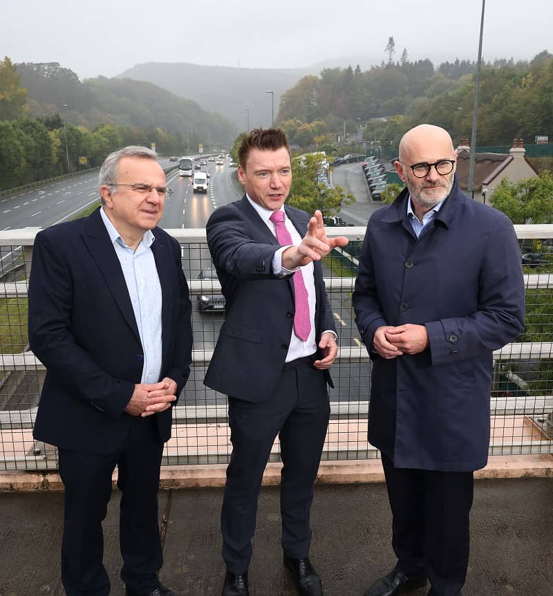 Eoin McManus speaks with two people spearheading the new Emerald Motorway Corridor while standing on a motorway bridge overlooking the road.