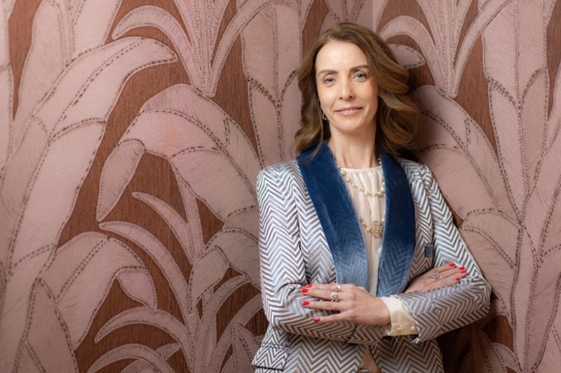 Elaine Carey, CEO of Three Ireland, smiling with arms crossed against a patterned wallpaper backdrop.