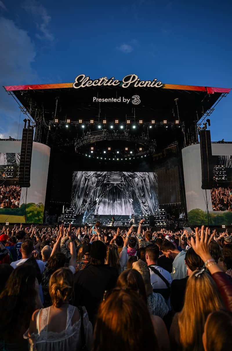 A vertical view from within a cheering crowd facing the illuminated main stage at the Electric Picnic music festival at dusk.