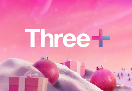 The "Three+" logo in white text with a pink and blue plus sign, overlaid on a festive pink background with snowy hills, pink Christmas ornaments, and wrapped gifts.